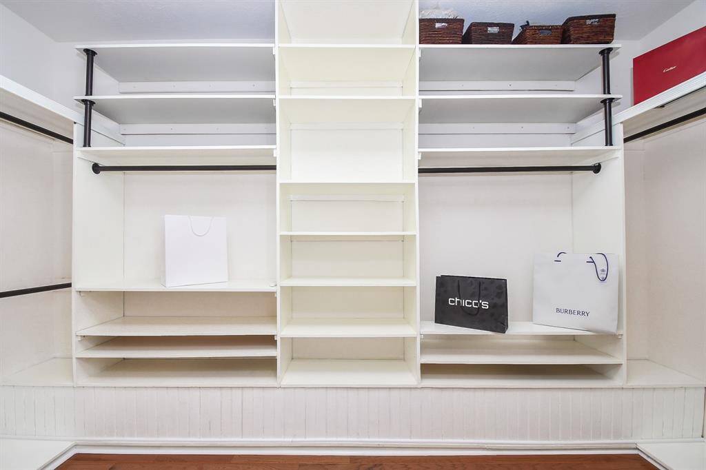 This photo shows a spacious walk-in closet with white shelving and racks, providing ample storage for clothing and accessories. The closet features multiple shelves, hanging rods, and storage baskets, offering organized and versatile storage options.