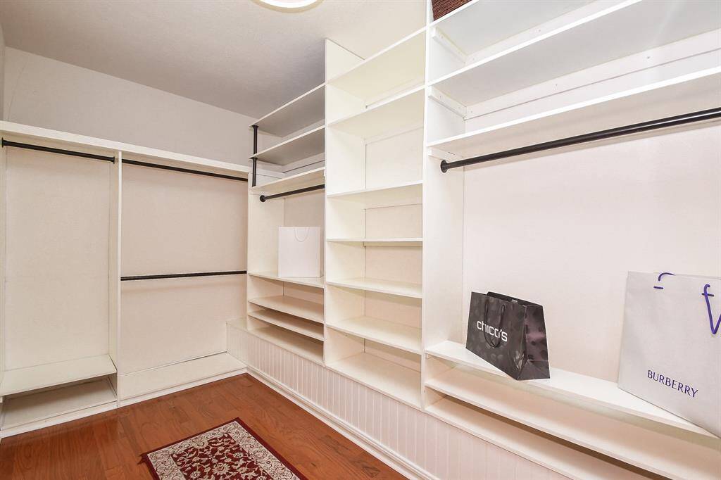 This photo shows a spacious walk-in closet with ample shelving and hanging space, featuring hardwood floors and a clean, organized look. Ideal for keeping your clothing and accessories neatly stored.