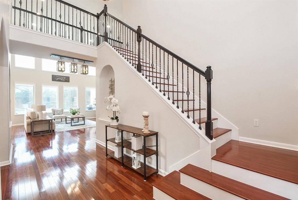 This inviting home features a bright, open living area with high ceilings and large windows, offering abundant natural light. The elegant staircase with wrought iron balusters adds a touch of sophistication, while the gleaming hardwood floors enhance the warm, welcoming atmosphere.