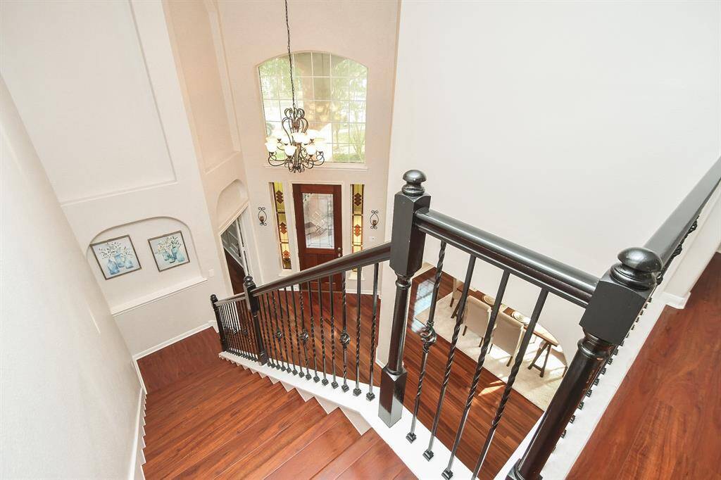 This photo showcases a bright and open stairway with elegant dark wood railings and polished wood steps. A large window and chandelier enhance the natural light, and the front door features custom made stained-glass panels with design matching the door. The space has a welcoming and spacious feel, perfect for a stylish entryway.