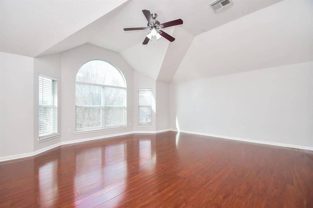 Bright and spacious game room with vaulted ceilings, large arched windows, hardwood flooring, and a ceiling fan. The game room has enough space for a pool table or can be used as a workout area.