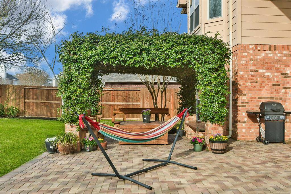 This inviting backyard features a spacious patio with a pergola covered in lush greenery, perfect for outdoor relaxation. Large windows enhance the home's exterior, providing ample natural light inside. Ideal for entertaining or enjoying peaceful moments outdoors.