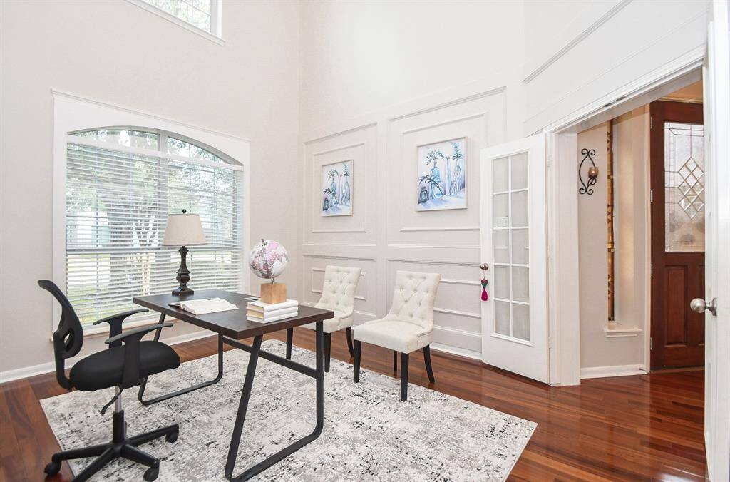Bright home office has high ceilings and features a large window for natural light. The home office has wood flooring, custom bookcase, moldings on the wall with French doors, creating a welcoming work environment.