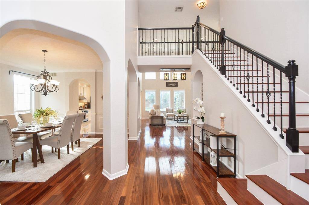 This photo showcases a spacious, open-concept home with elegant hardwood floors and a grand staircase. The dining area features an ornate chandelier, while large windows in the living room provide ample natural light. The design is modern and inviting, perfect for both entertaining and family living.