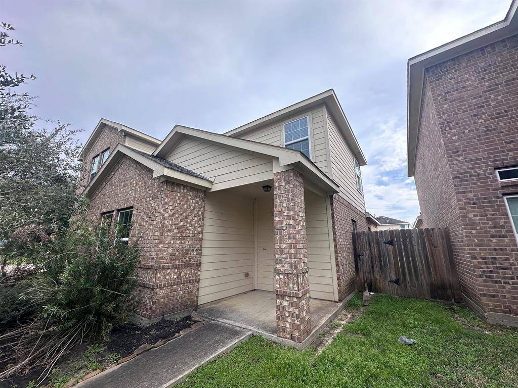 This photo showcases a two-story brick and siding home with a covered front entry and a partially visible wooden fence. The exterior has a modest lawn and some foliage, offering a welcoming suburban feel.