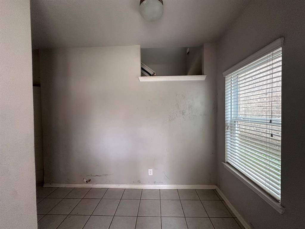 This room features neutral walls, tiled flooring, and a large window with blinds for natural light. There's a small ledge above the wall, adding architectural interest. Potential for customization.