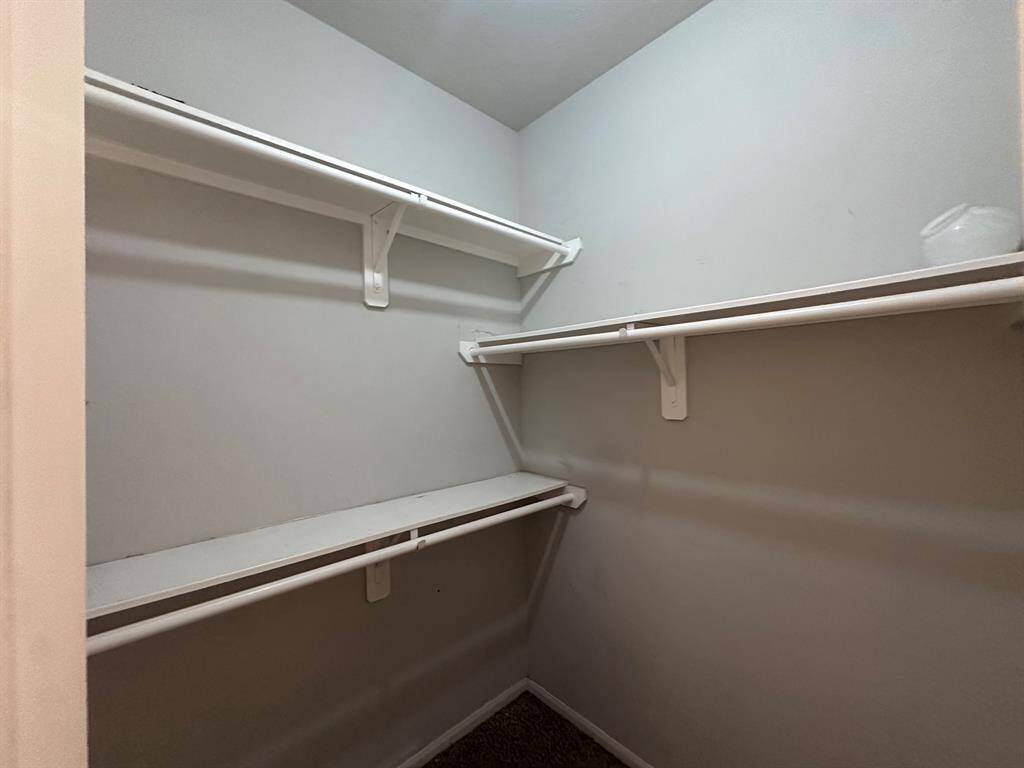 This is a spacious walk-in closet featuring multiple white shelves and hanging rods, ideal for organizing clothing and accessories. The neutral walls and carpeted floor provide a clean and versatile space.