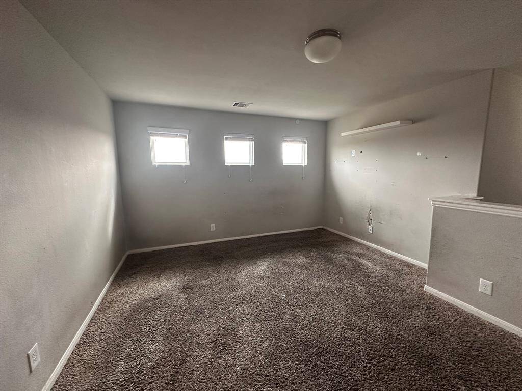 This room features neutral walls, three small windows for natural light, and carpeted flooring. There's a ceiling light fixture and a partial wall, creating a cozy, versatile space.