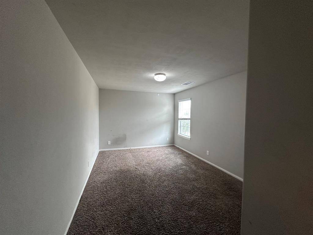 This room features neutral-toned walls, carpet flooring, and a ceiling light. A window on one side allows natural light to enter, creating a cozy atmosphere. Perfect for a bedroom or home office.