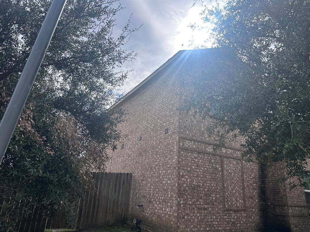 Brick exterior of a two-story home with a wooden fence and mature trees providing shade. The sun is peeking through the branches, creating a serene atmosphere.