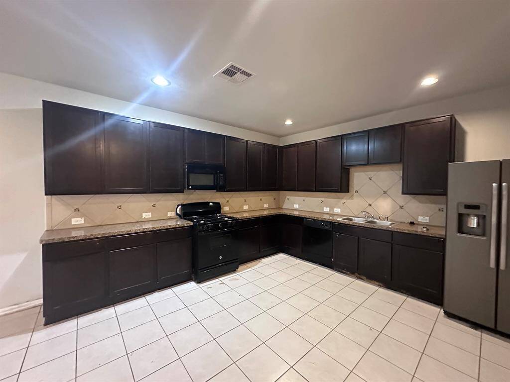 Spacious kitchen with dark cabinetry, tiled backsplash, and modern appliances, including a large refrigerator and gas stove. Ample counter space and tile flooring enhance functionality.