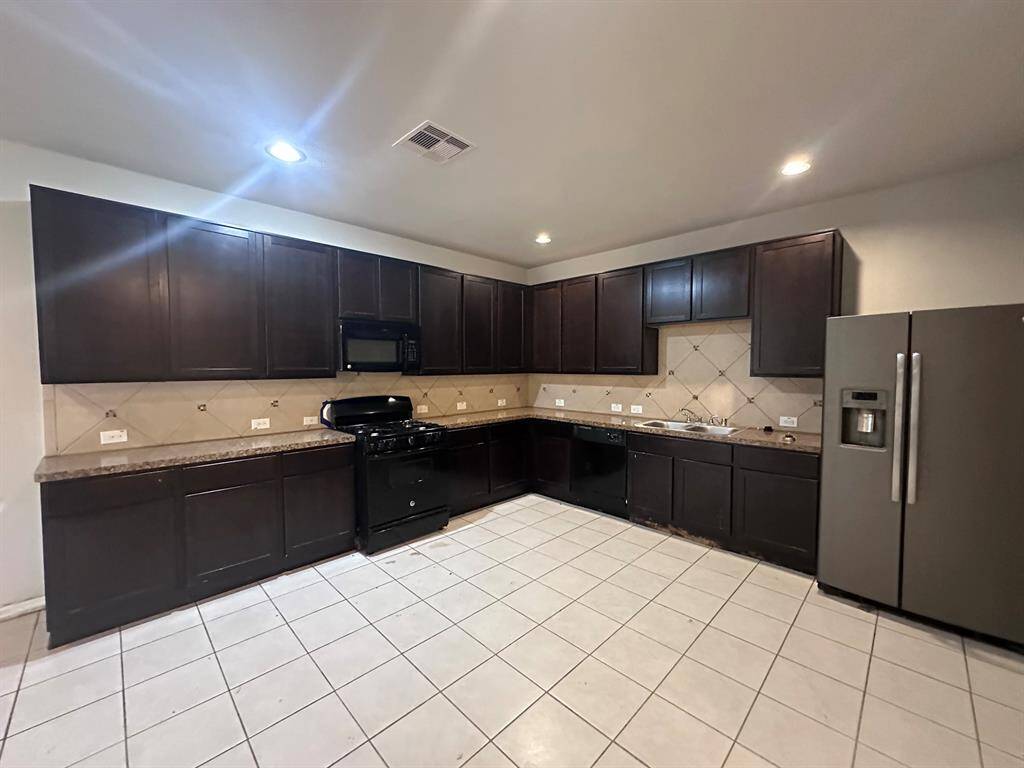 Spacious kitchen with dark cabinets, tiled backsplash, and floor. Features modern appliances, including a fridge, oven, and microwave. Bright lighting enhances the clean, contemporary design.