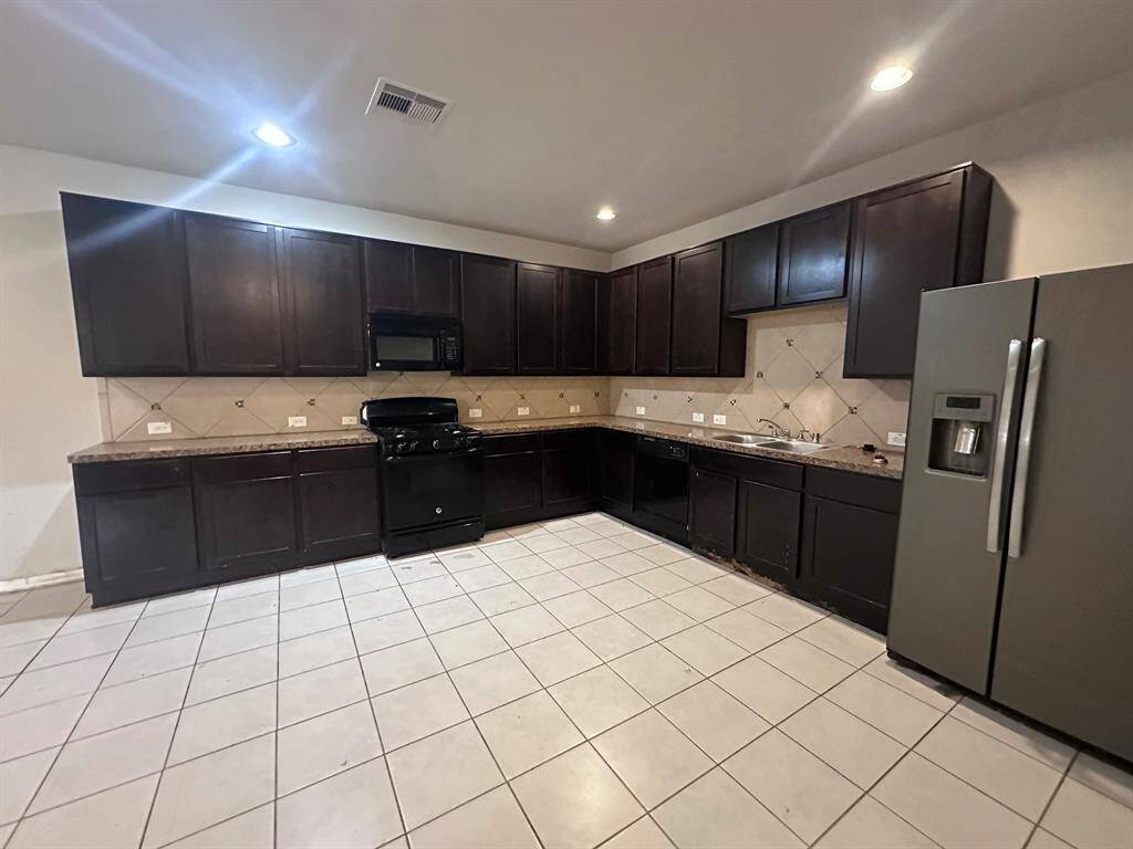 Spacious kitchen featuring dark cabinets, granite countertops, and tiled floors. Equipped with stainless steel appliances, including a refrigerator and dishwasher, plus a built-in microwave. The layout offers plenty of storage and workspace.