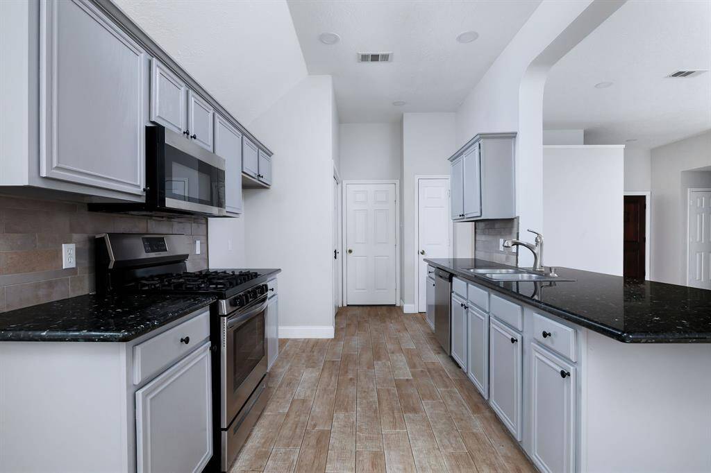 This kitchen features sleek black granite countertops, light gray cabinetry, and stainless steel appliances. Open concept looking out to living room and backyard!