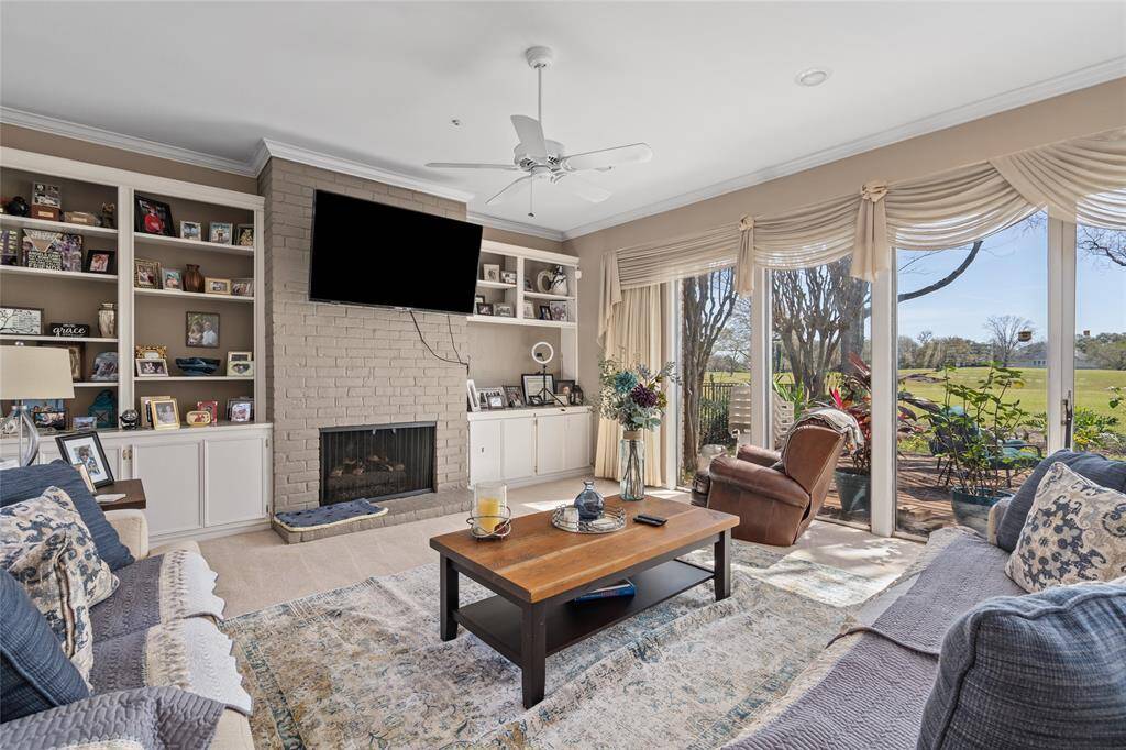 This inviting living space boasts a beautiful brick fireplace, flanked by built-in shelving for storage and display. Floor-to-ceiling windows provide breathtaking views of the lush golf course, filling the room with natural light. The neutral tones and crown molding add a touch of elegance, while the open layout makes it a perfect gathering spot.