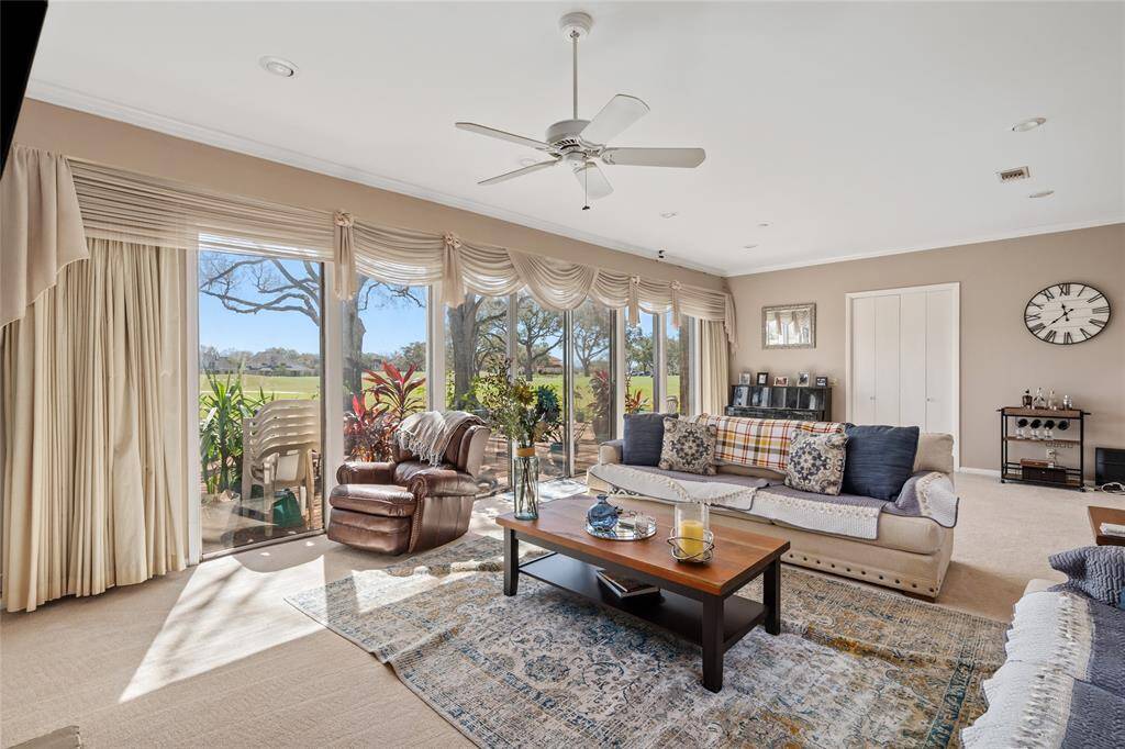 This spacious living room offers a warm and inviting atmosphere, featuring large windows that frame the backyard pergola and patio area. Plush carpeting, soft neutral tones, and elegant crown molding enhance the room’s charm, while the open layout provides flexibility for entertaining or relaxing.