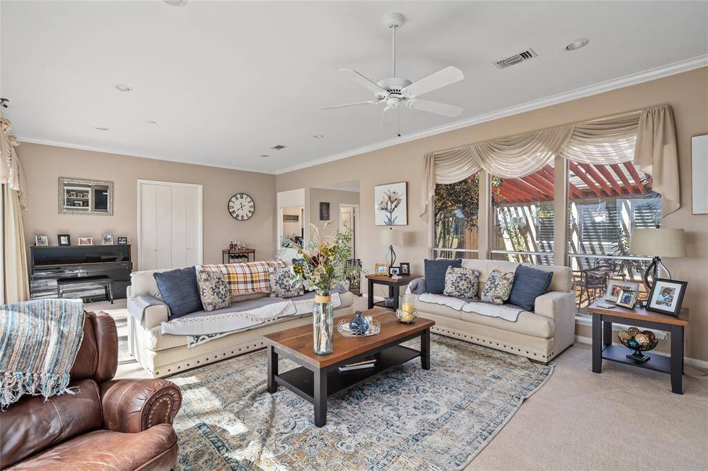 Flooded with natural light, this expansive living room offers stunning views of the lush golf course through a wall of floor-to-ceiling windows. The neutral color palette, plush carpeting, and elegant window treatments create a warm and inviting atmosphere, perfect for both relaxation and entertaining.