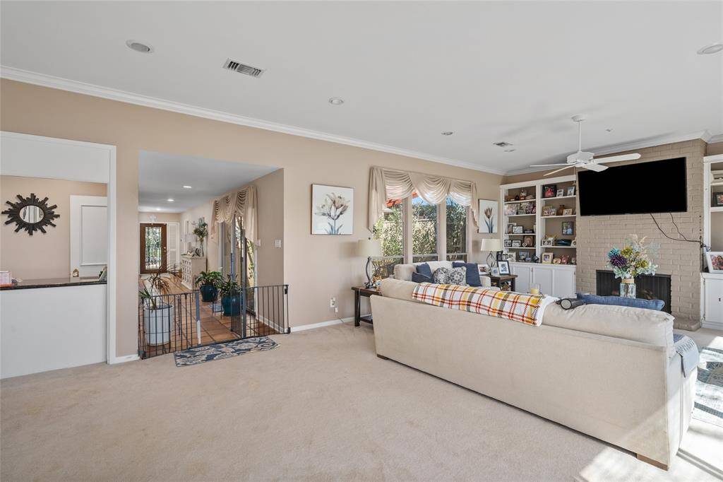 This spacious living area offers a cozy yet open feel, featuring a brick fireplace framed by built-in shelving for storage and display. Large windows allow for abundant natural light, while the neutral color palette and plush carpeting create a welcoming atmosphere. The room seamlessly connects to the foyer and kitchen, enhancing the home's flow.