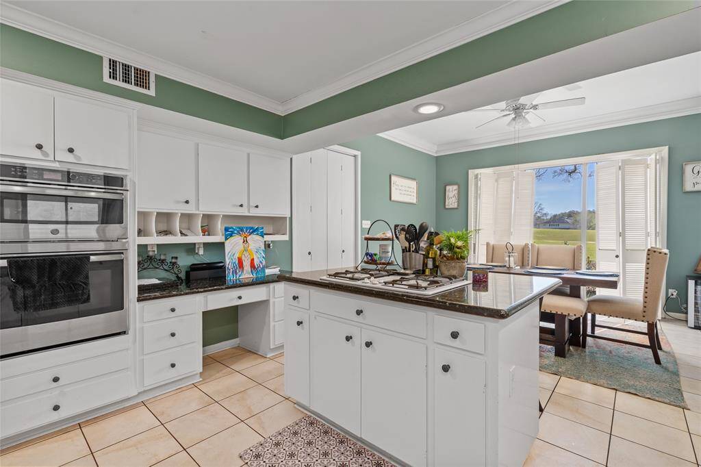 This inviting kitchen features ample cabinetry, a built-in oven, and a spacious island with a gas cooktop. The convenient built-in desk area offers additional storage and workspace. Large windows in the adjacent dining area provide stunning views, filling the space with natural light.