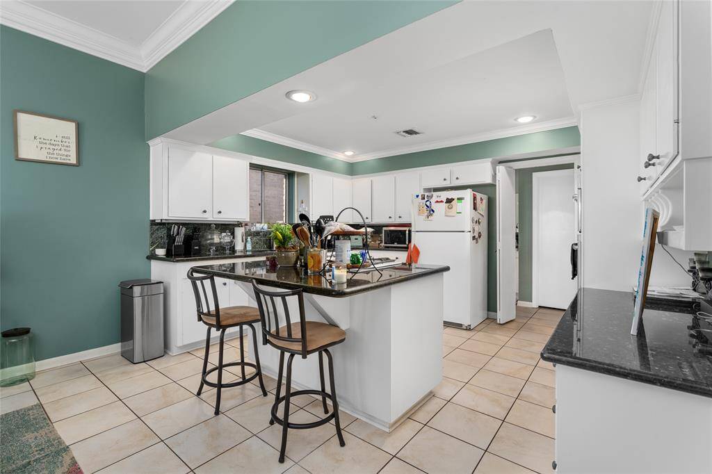 This spacious kitchen features a large central island with bar seating, providing both functionality and a casual dining option. The white cabinetry offers ample storage, while the granite countertops add a sleek and polished touch. Recessed lighting and crown molding enhance the space, creating a bright and inviting atmosphere.