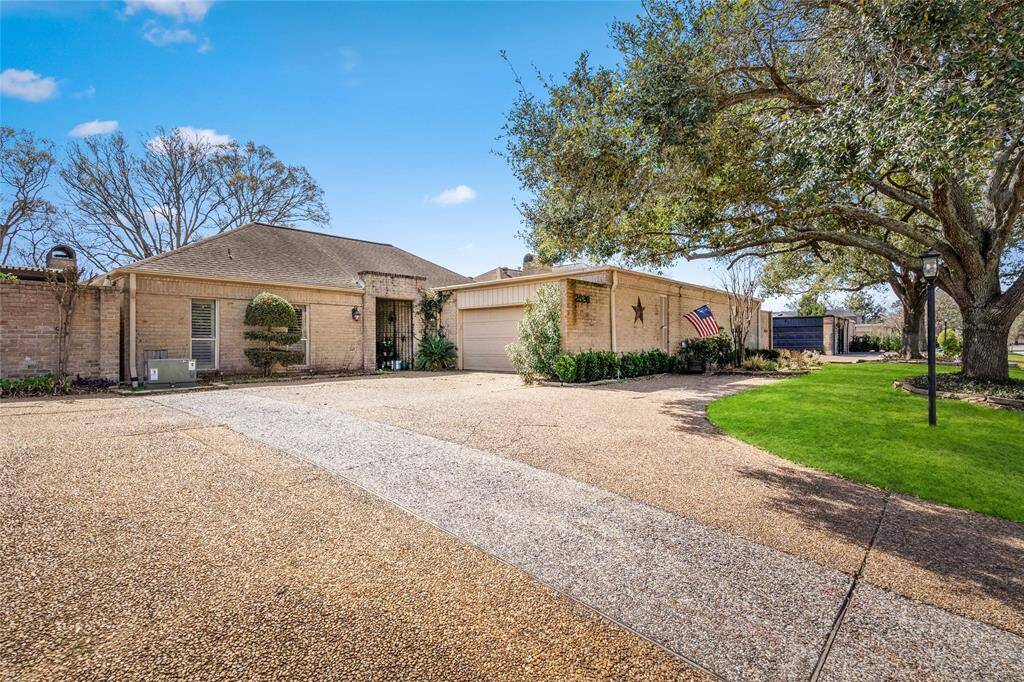 This exterior view showcases a well-maintained, single-story home with a spacious driveway and attached garage. Mature trees provide shade, while the landscaped front yard adds to the home's curb appeal. The entryway is set back for added privacy, and outdoor lighting enhances the welcoming atmosphere.