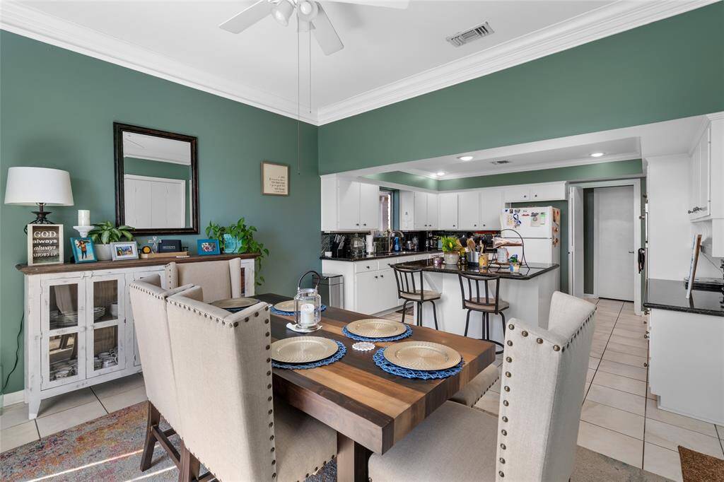 This open-concept dining and kitchen area offers a welcoming and functional space for entertaining. The dining area features a rich wooden table with seating for six, while the adjacent kitchen boasts a spacious island with additional bar seating. White cabinetry, granite countertops, and recessed lighting enhance the kitchen’s modern appeal, while the green accent walls and crown molding add warmth and character.