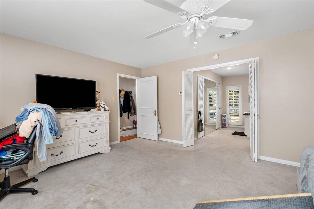 The primary bedroom features an en-suite area with a walk-in closet and additional space that can be used as a dressing area or sitting nook. Double doors open up to this versatile space, while another doorway provides easy access to the rest of the home. Neutral tones and soft carpeting create a cozy and inviting atmosphere.