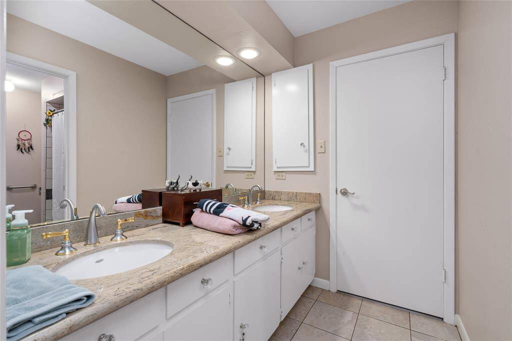 This secondary bathroom features a spacious dual-sink vanity with a granite countertop and ample cabinet storage. A large mirror enhances the brightness of the space, complemented by recessed lighting. The neutral color palette and tiled flooring create a clean and inviting atmosphere. A separate bathing area with a tiled shower adds functionality and privacy.