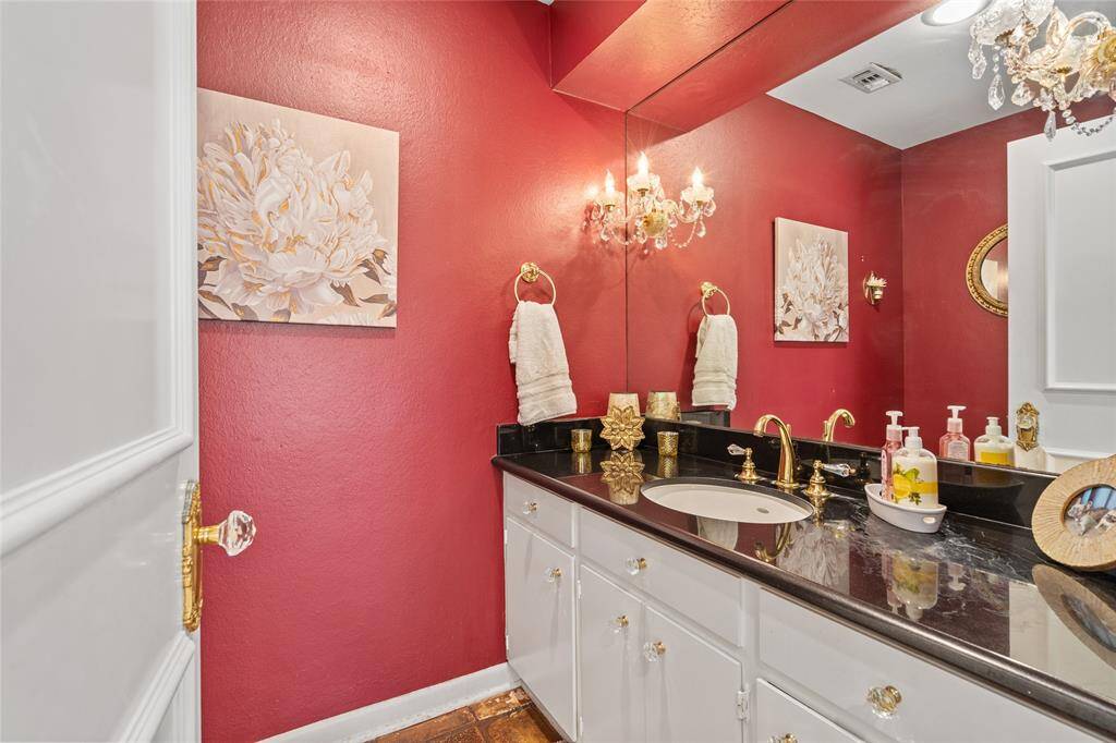 This elegant half bath makes a bold statement with rich red walls, a sleek black granite countertop, and gold fixtures adding a touch of sophistication. The oversized mirror enhances the space, while crystal-accented lighting provides a warm, inviting glow. Perfect for guests to use, this stylish powder room offers both charm and functionality!