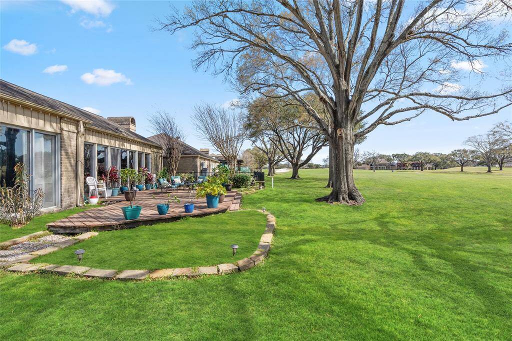 Expansive backyard retreat with a spacious wooden deck, seamlessly blending into the lush greenery of the golf course. Mature trees provide natural shade, while the landscaped stone pathway and garden beds add character to the outdoor space. A perfect setting for relaxation and enjoying scenic views.