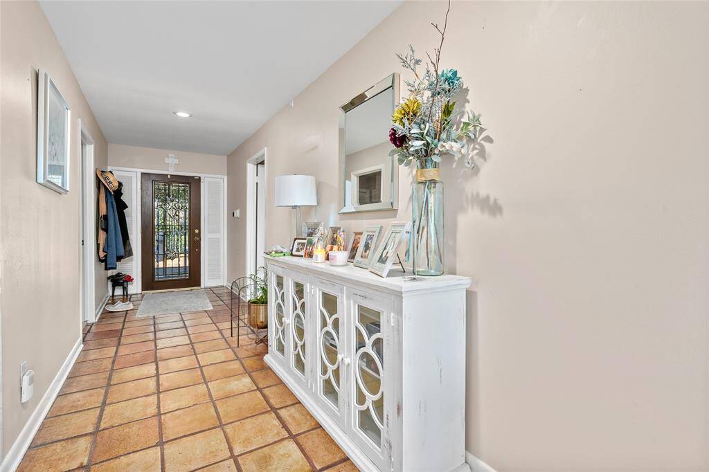 The inviting entryway features warm-toned tile flooring and neutral walls, creating a welcoming atmosphere. A decorative glass-paneled door allows natural light to brighten the space. The hallway offers ample room for décor and storage, setting the perfect first impression for this charming home.