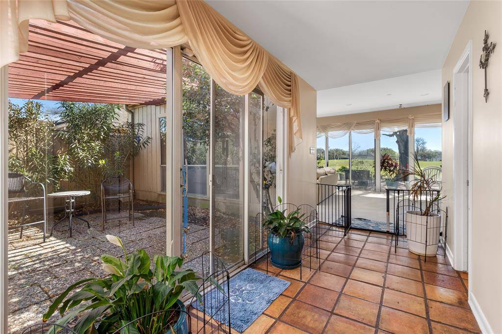 This bright and airy hallway features large sliding glass doors that open to a private center courtyard, allowing natural light to flow into the space. The courtyard offers a peaceful outdoor retreat with a paved patio and lush greenery. Further down, the hallway leads to a living area with expansive windows showcasing scenic views.