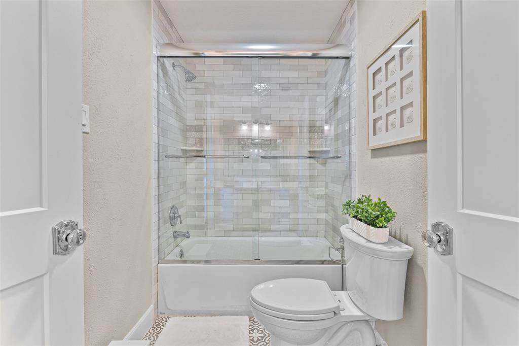 This bathroom has a tile surround tub/shower combo with glass rolling doors.