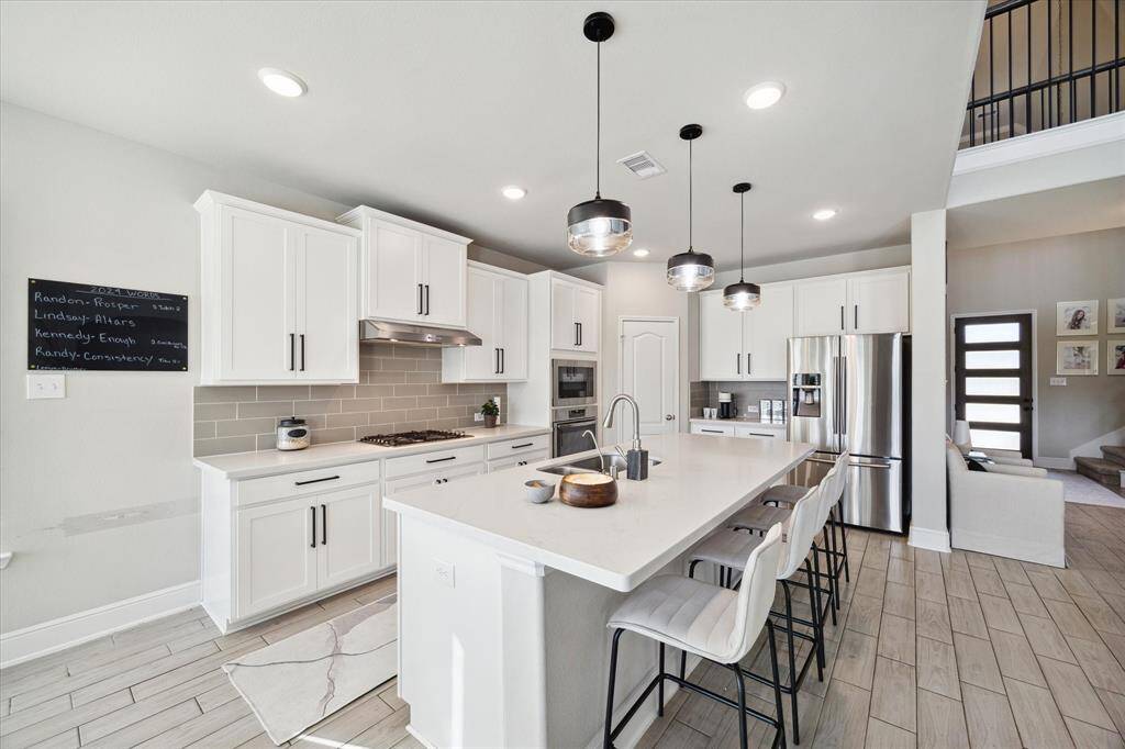 This modern kitchen features sleek white cabinetry, a large island with seating for 5, stainless steel appliances, and pendant lighting. The open layout connects to a cozy living area with natural light and stylish decor.