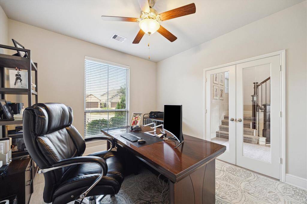 This bright home office with a large window offers natural light.  The room is accessible through elegant glass French doors, providing a view of the staircase.
