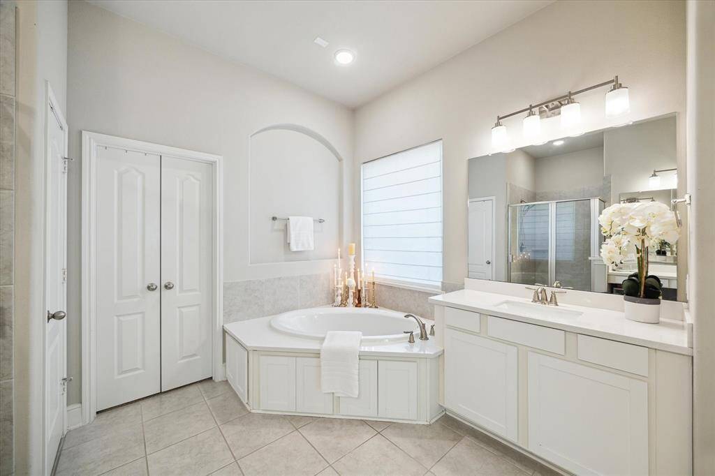 This bathroom features a spacious design with a large soaking tub, separate shower, dual sinks, and ample storage. The neutral color palette and elegant lighting create a bright and inviting atmosphere.