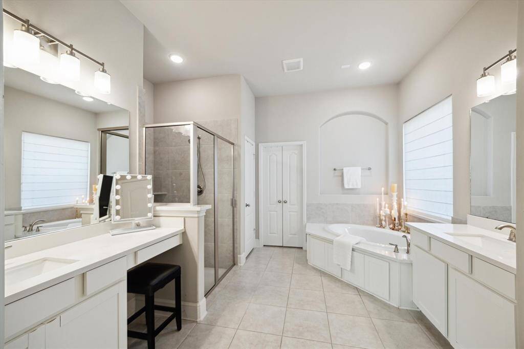 This spacious bathroom features modern lighting, a large vanity with a makeup vanity, a glass-enclosed shower, and a luxurious soaking tub. The neutral color palette and ample natural light create a serene atmosphere.