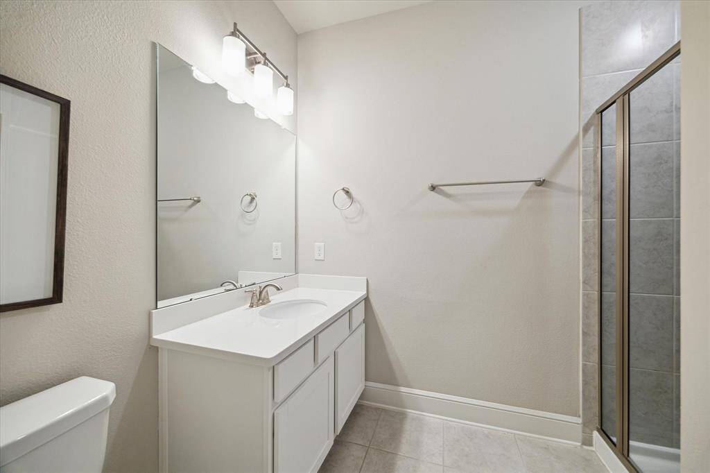 This is a modern, clean bathroom featuring a single sink vanity with ample storage, a large mirror, and bright overhead lighting. It includes a glass-enclosed shower with tile accents and neutral-toned walls and flooring, creating a fresh and inviting space.