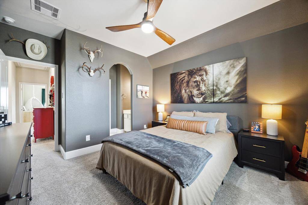 This cozy secondary bedroom features a neutral color scheme with gray walls and carpet, a stylish ceiling fan, and ambient lighting. The room has a Hollywood bathroom and a welcoming atmosphere that overlooks the front of the home.