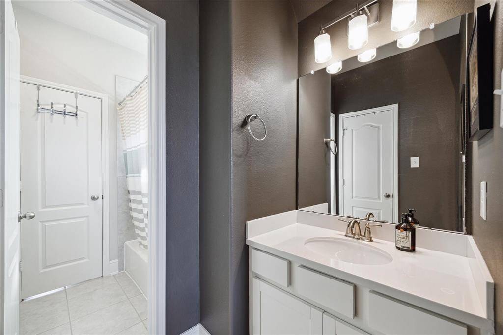 This Hollywood bathroom features a modern design with dark walls and a white countertop. It includes a large mirror with stylish lighting and a door leading to a shower area.