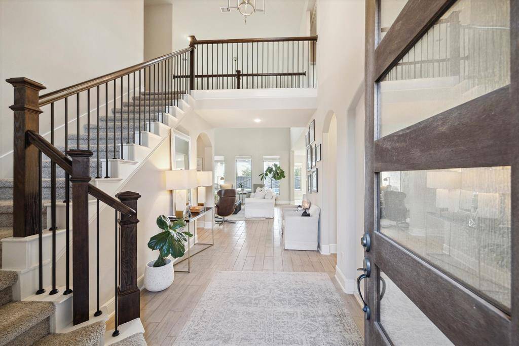 This inviting home features a spacious entryway with elegant wood and iron staircase, leading to a bright, open living area. The interior boasts neutral tones, modern decor, and ample natural light, creating a warm and welcoming atmosphere.
