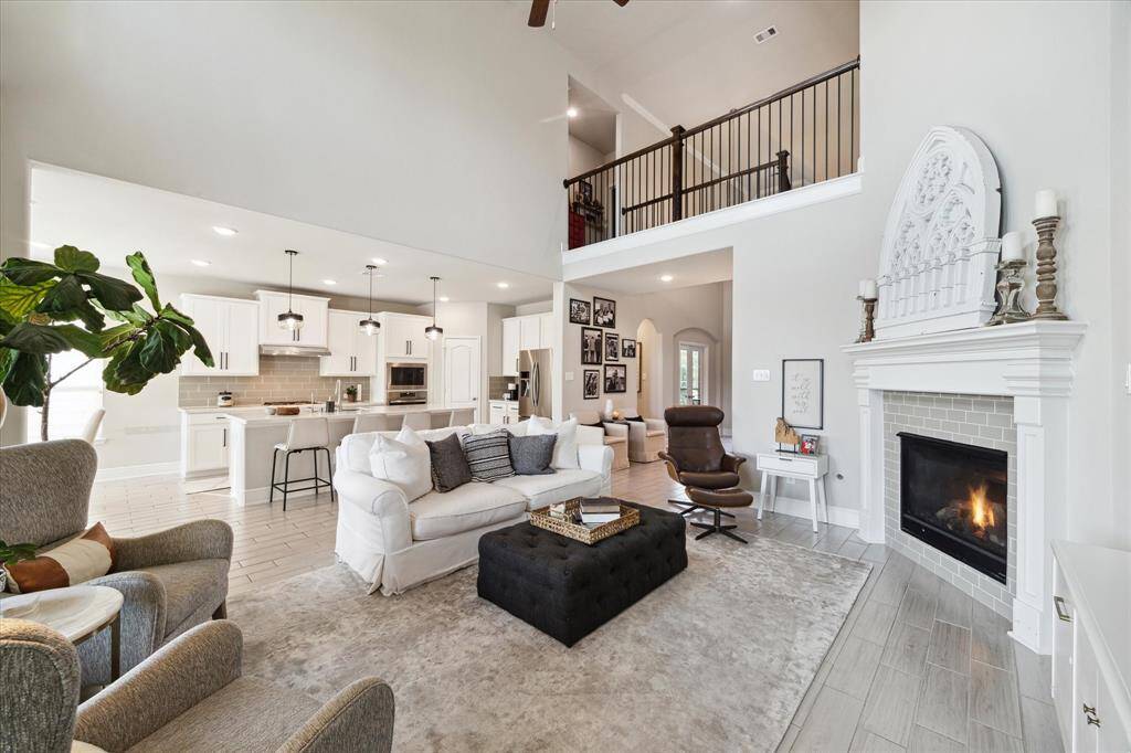 This spacious living area features an open floor plan with high ceilings and a modern kitchen. It includes a cozy fireplace, elegant decor, and a second-floor balcony overlooking the space, creating a welcoming and stylish atmosphere.