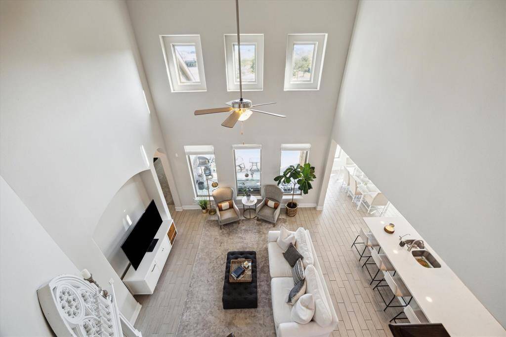 This photo showcases a modern, open-concept living area with high ceilings and abundant natural light from large windows. The space features a cozy seating arrangement, a sleek TV setup, and a kitchen island with bar seating, creating an inviting atmosphere for relaxation and entertainment.