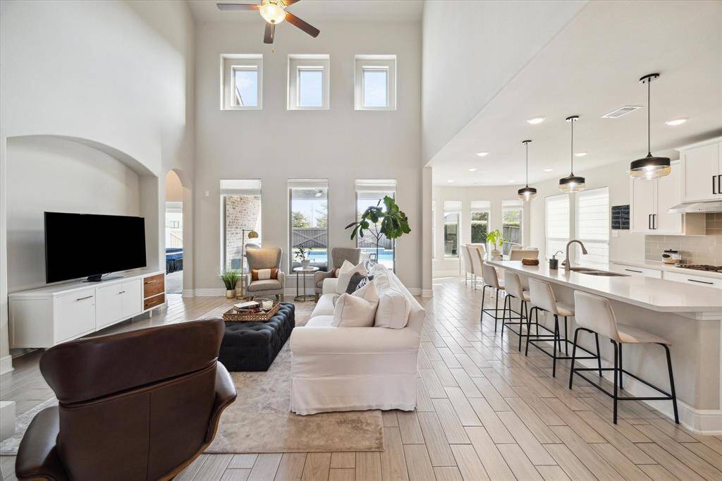 This spacious living area features high ceilings, abundant natural light from tall windows, and an open floor plan connecting to a modern kitchen with a large island and sleek finishes. Ideal for entertaining, the space is both elegant and inviting.