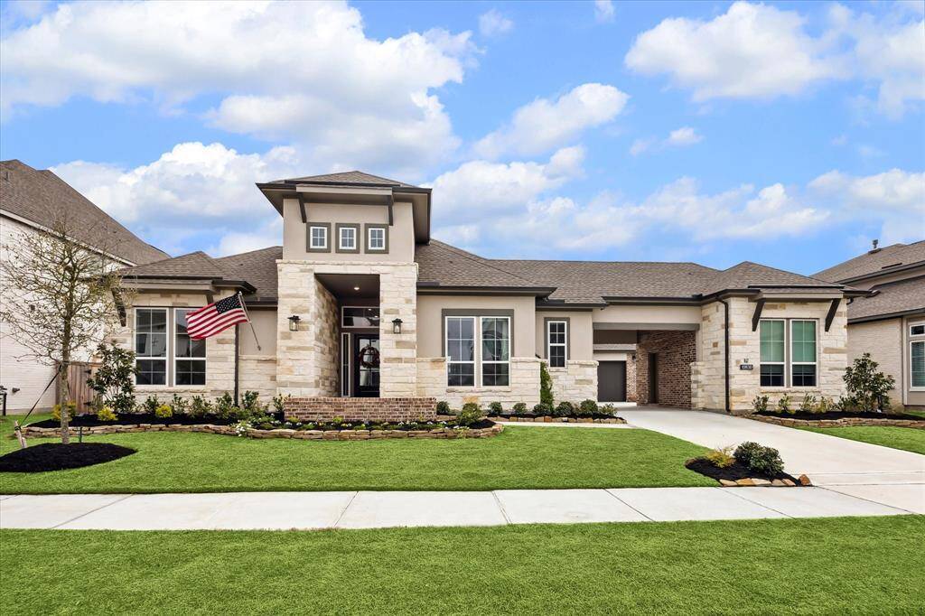 This modern single-story home features an elegant façade with a blend of stone and stucco, complemented by large windows and a beautiful front yard.