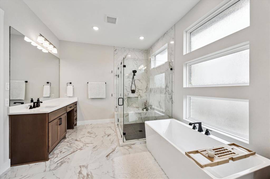 Primary bathroom with a freestanding bathtub, and dual sinks with a large mirror. Natural light pours in through frosted windows.