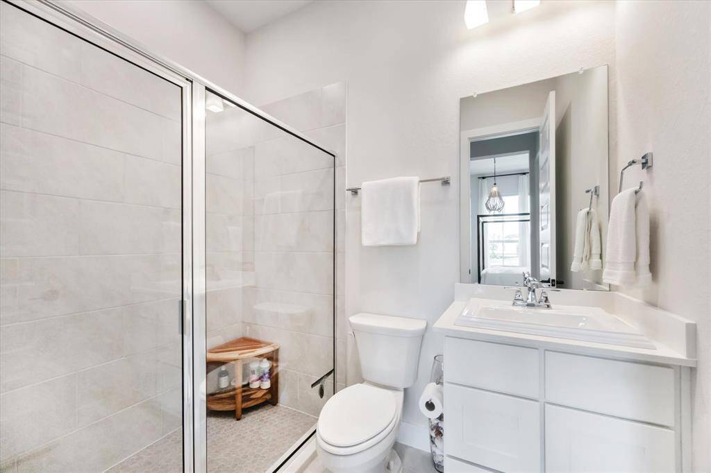 This bathroom offers a modern design with a spacious glass-enclosed shower, sleek white vanity, and bright lighting, creating a fresh and inviting space.