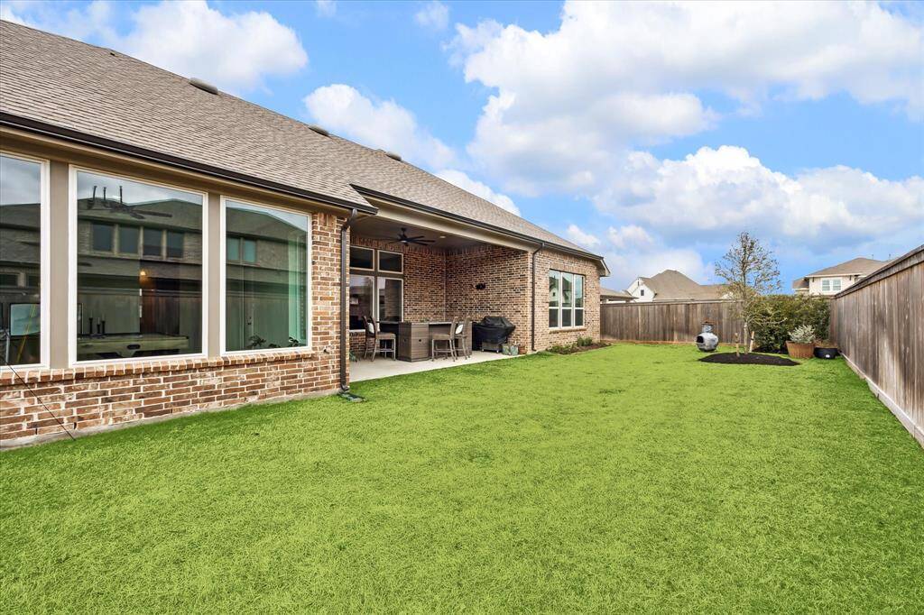 A spacious backyard with lush green grass, a brick exterior home, large windows, and a covered patio area, perfect for outdoor entertaining.