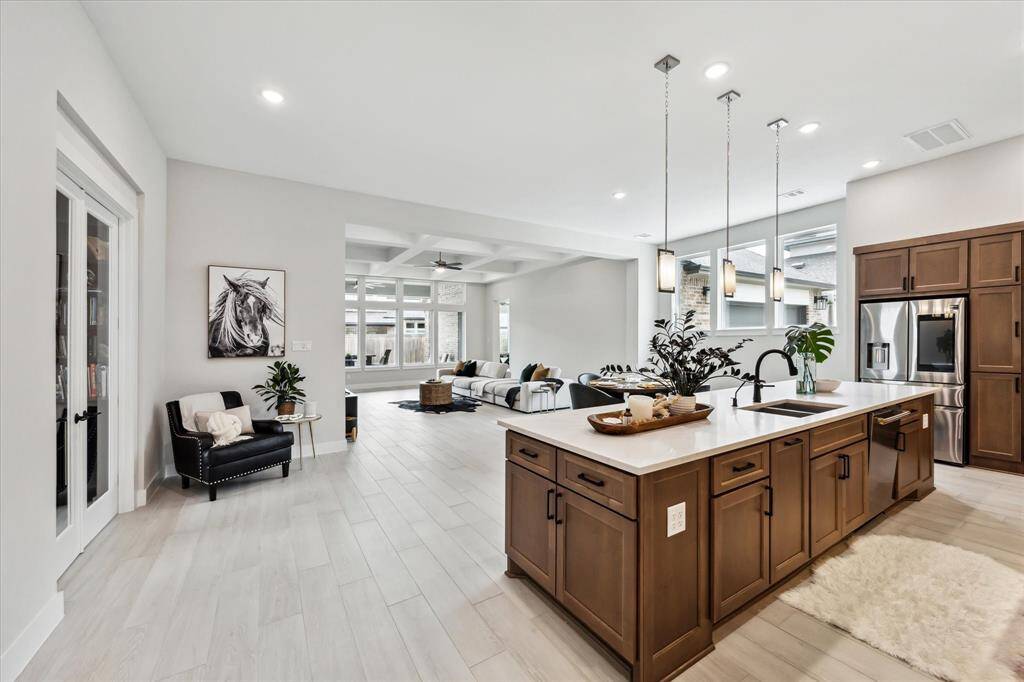 Modern open-concept living area with a sleek kitchen island, stainless steel appliances, and ample natural light from large windows. The neutral color palette and contemporary finishes create an inviting and elegant atmosphere.