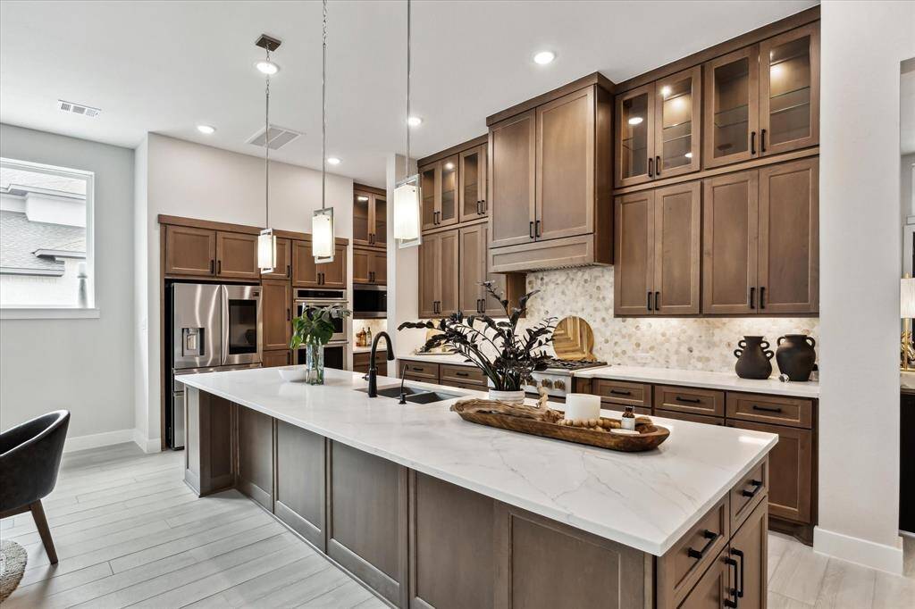 This kitchen features modern wood cabinets, a large island with pendant lighting, and stainless steel appliances. The space is bright with recessed lighting and a contemporary backsplash, providing a stylish and functional cooking area.